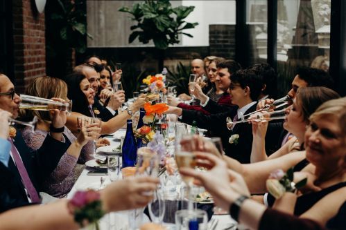 Family and friends gathered around the table in the Writer's Den Enclosed terrace toasting to the Bride and Groom. Photo by: Lauren Spinelli Photography